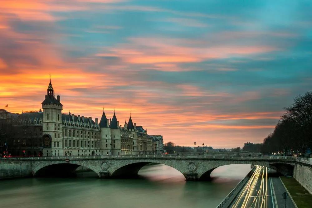 Puente sobre el río Sena con edificios históricos y un atardecer colorido.