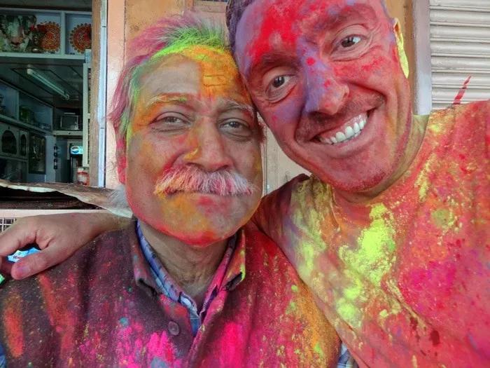 Dos hombres sonrientes cubiertos de polvos de colores brillantes.
