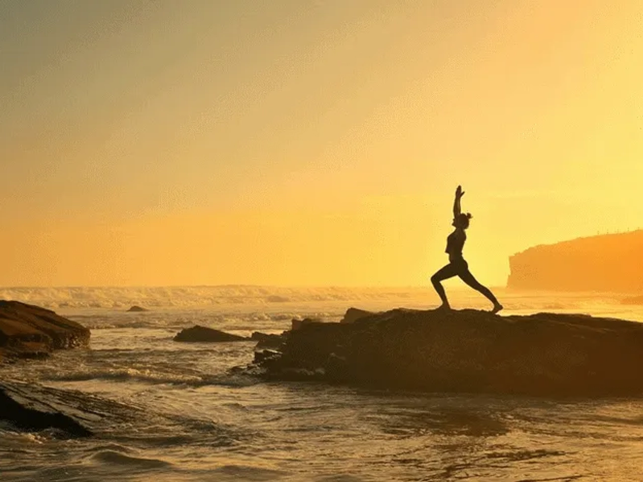 Silueta de una persona haciendo yoga en una roca frente al mar al atardecer.