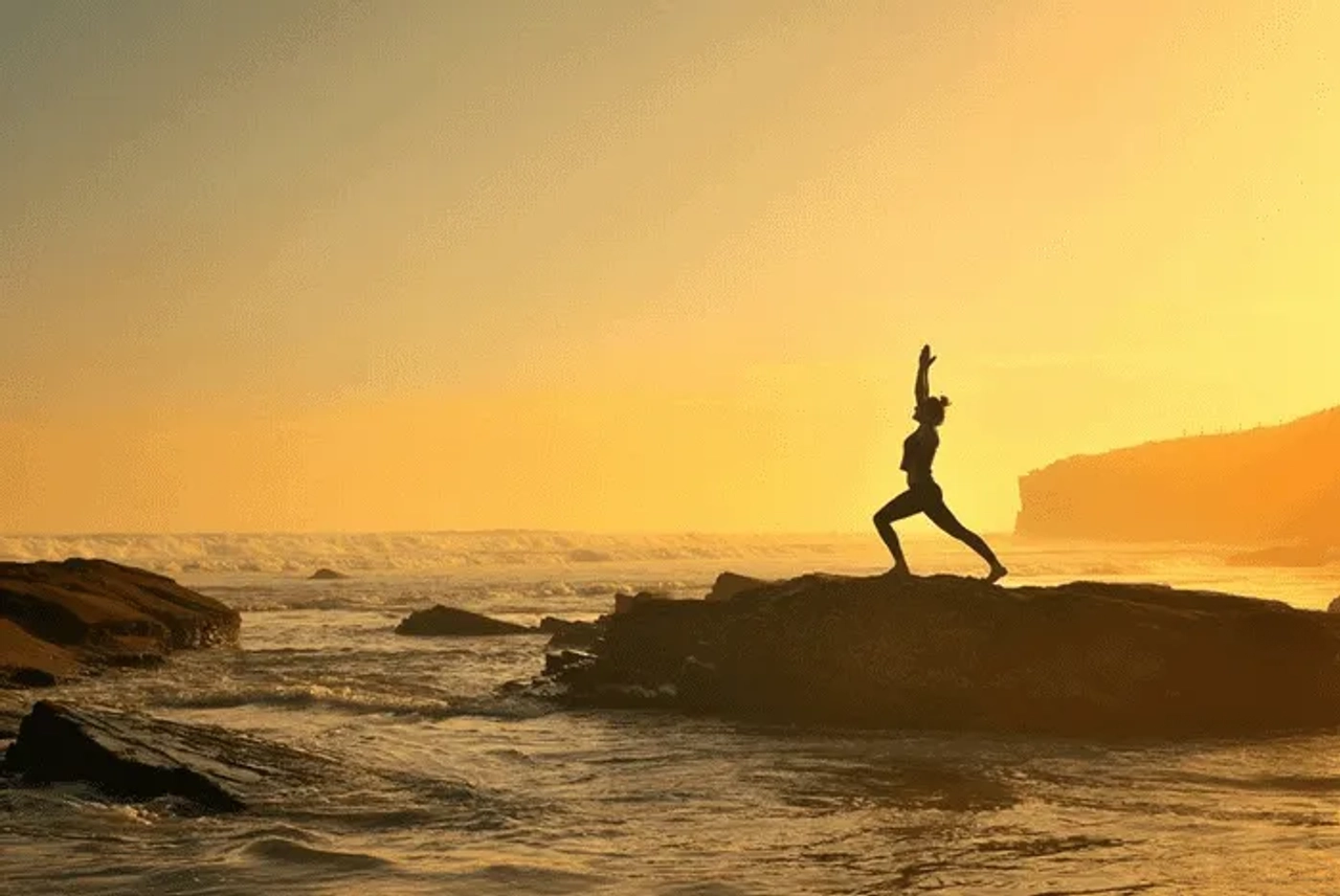 Silueta de una persona haciendo yoga en una roca frente al mar al atardecer.