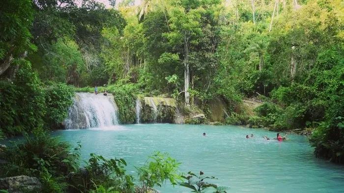 Cascada en un entorno natural, con personas disfrutando en el agua turquesa.