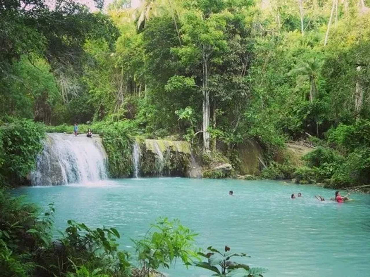Cascada en un entorno natural, con personas disfrutando en el agua turquesa.