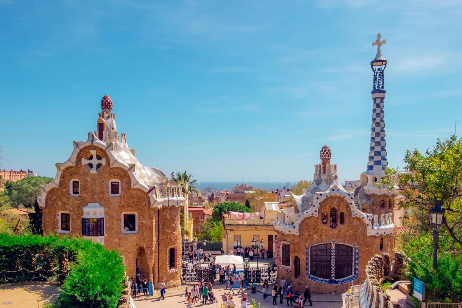 Colorful architectural structures in Park Güell, Barcelona, with visitors and a clear blue sky.