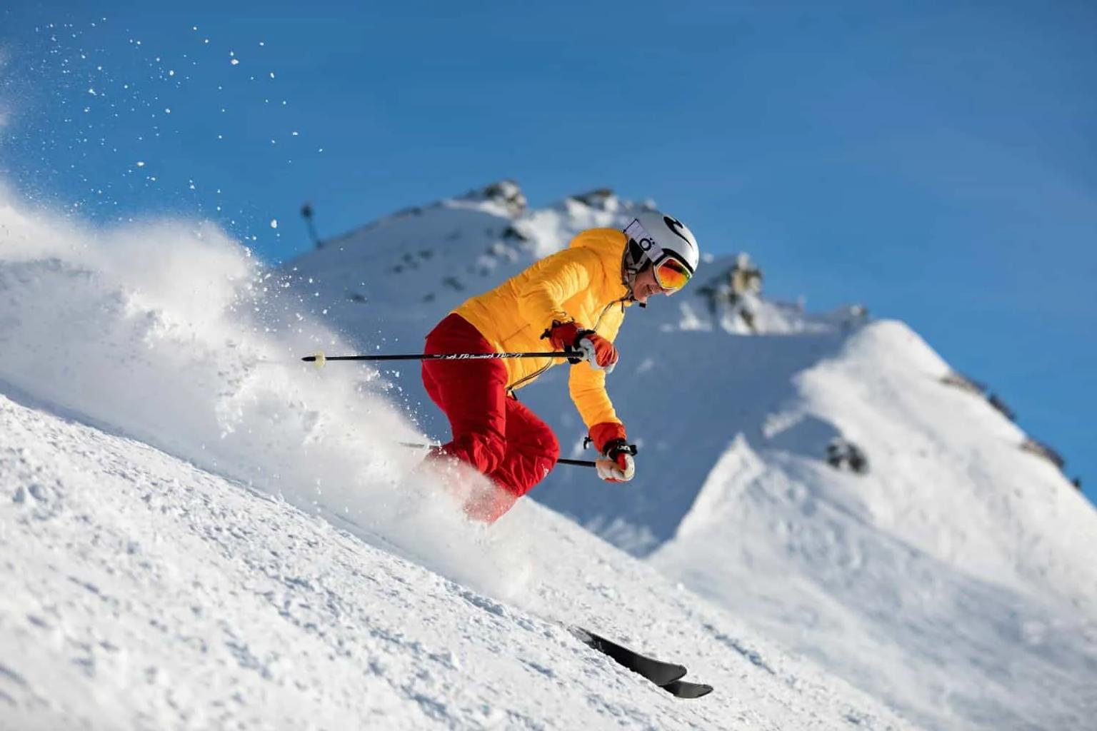 Esquiador descendo uma pista de neve em um dia ensolarado.