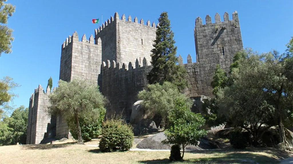 Castelo de Guimarães, monumento histórico cercado por vegetação e céu azul.