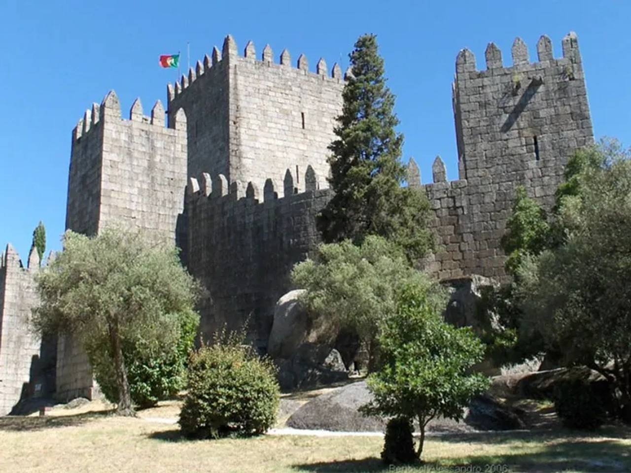 Castelo de Guimarães, monumento histórico cercado por vegetação e céu azul.