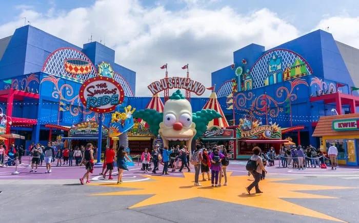 Entrada colorida de Krustyland, con atracciones y visitantes disfrutando del parque temático.