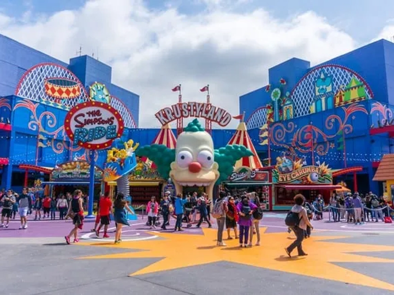 Entrada colorida de Krustyland, con atracciones y visitantes disfrutando del parque temático.