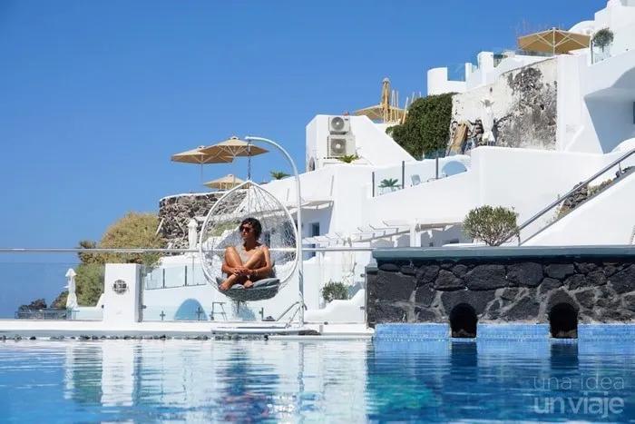 Persona sentada en una silla colgante junto a una piscina en un entorno soleado.