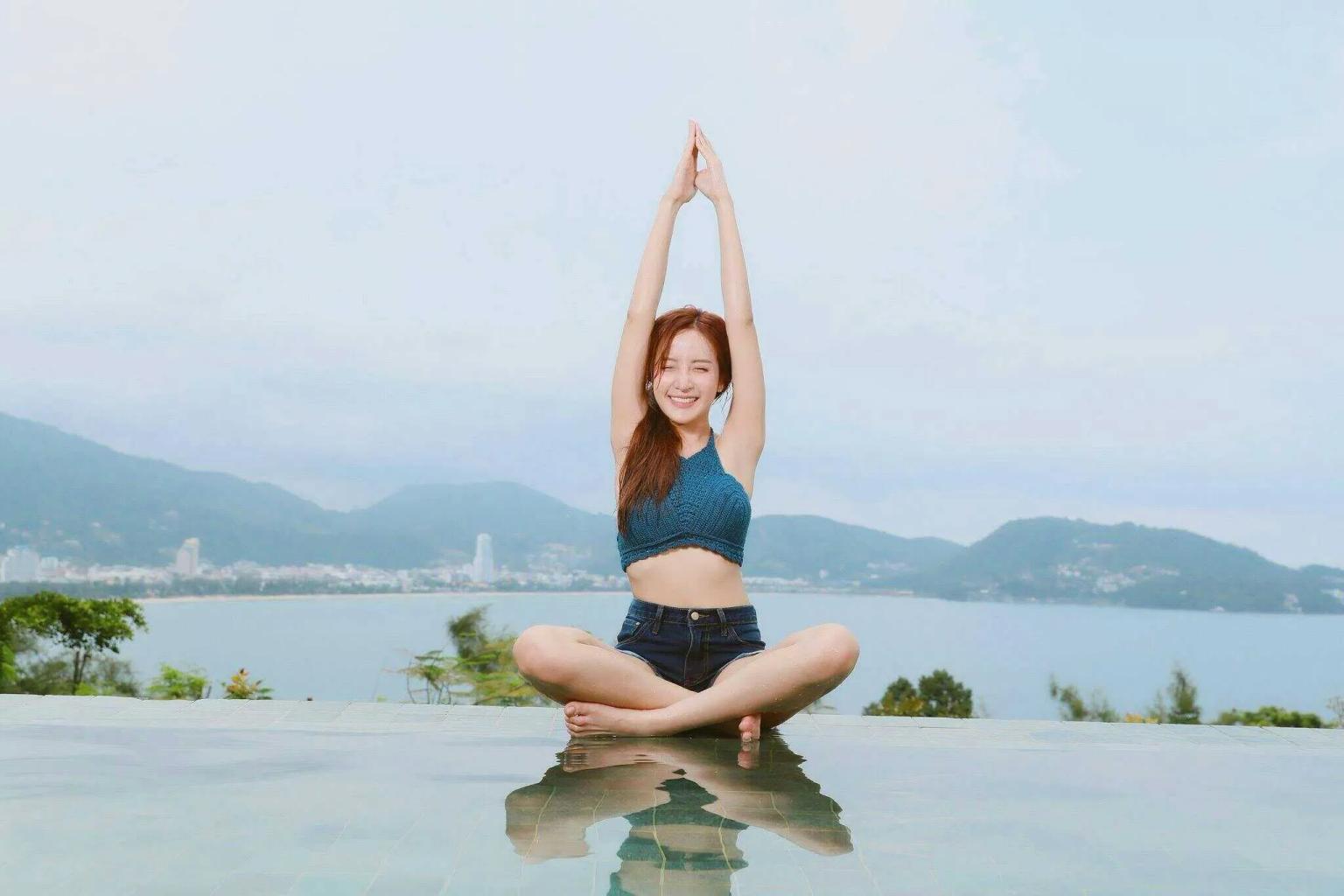 Mulher praticando yoga à beira de uma piscina com vista para montanhas e mar.