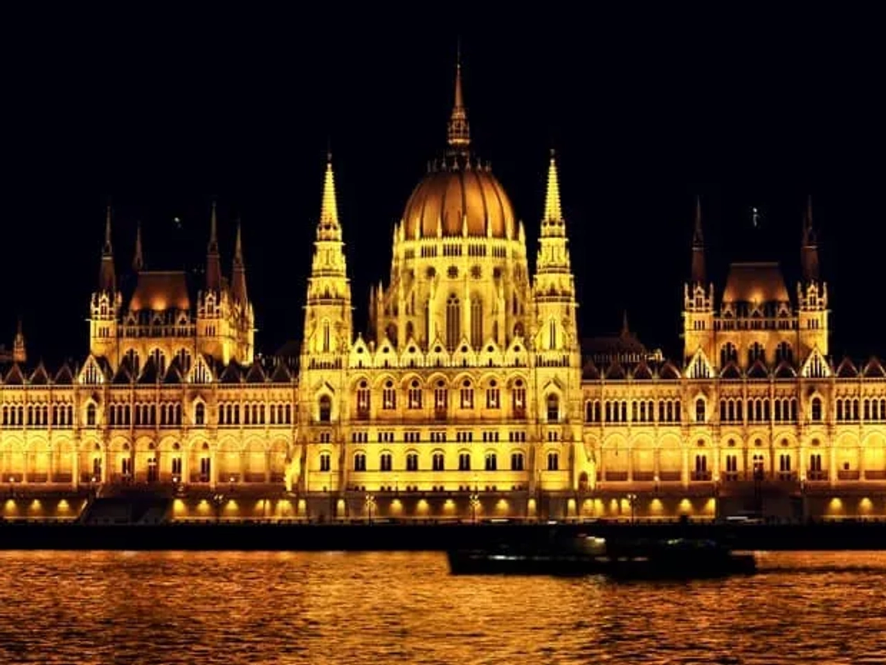 Edificio del Parlamento de Budapest iluminado por la noche, reflejándose en el agua.