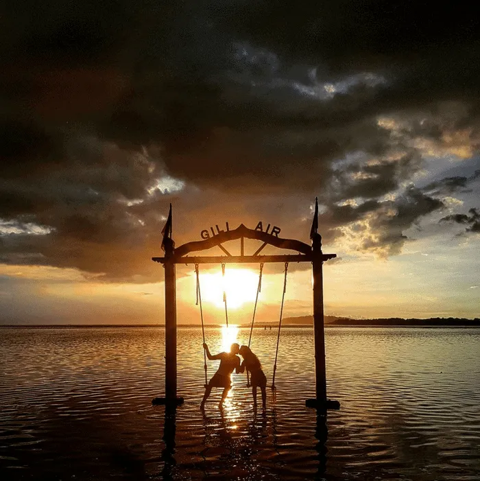 Pareja en un columpio frente a un atardecer en Gili Air.