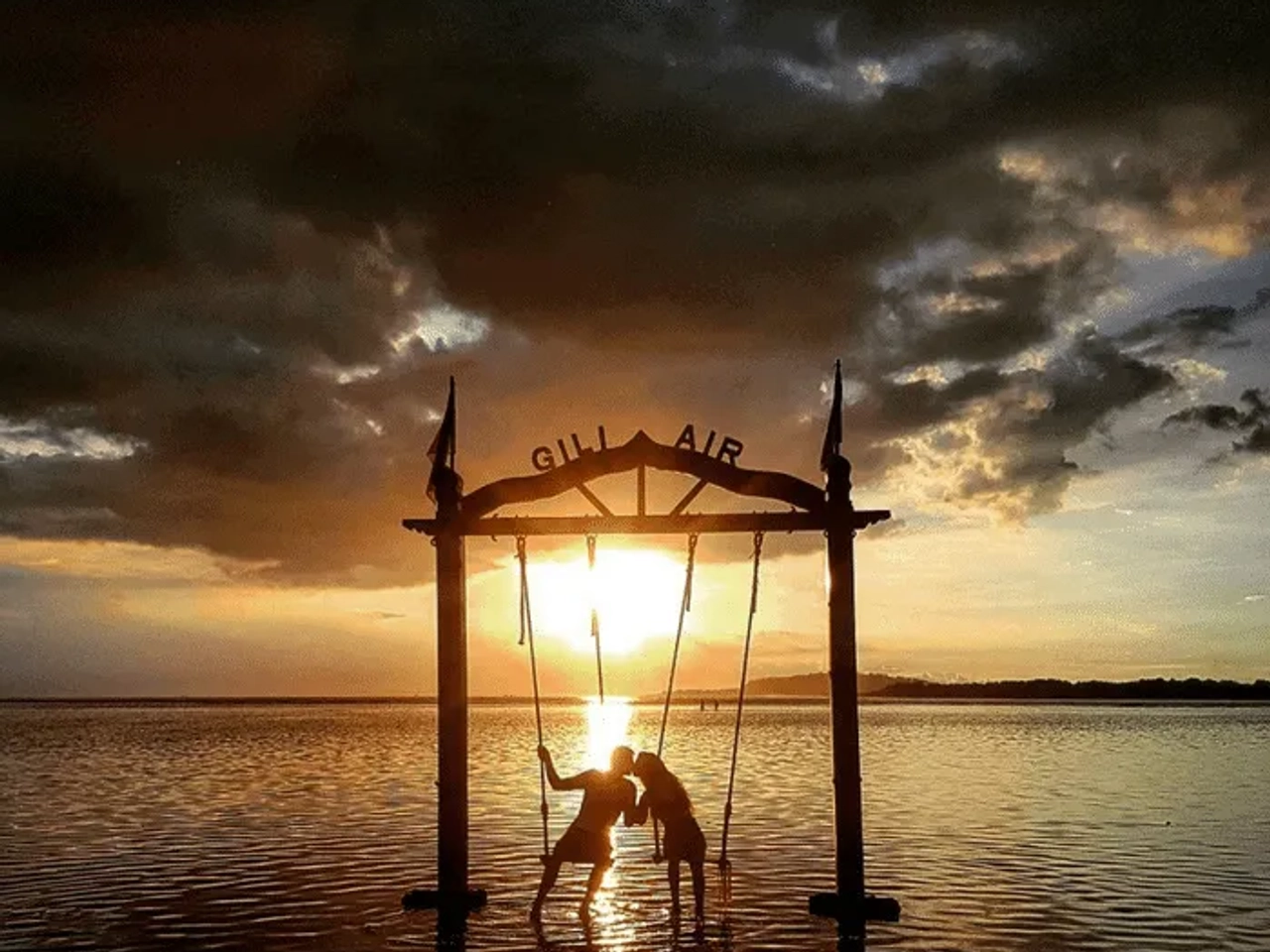 Pareja en un columpio frente a un atardecer en Gili Air.