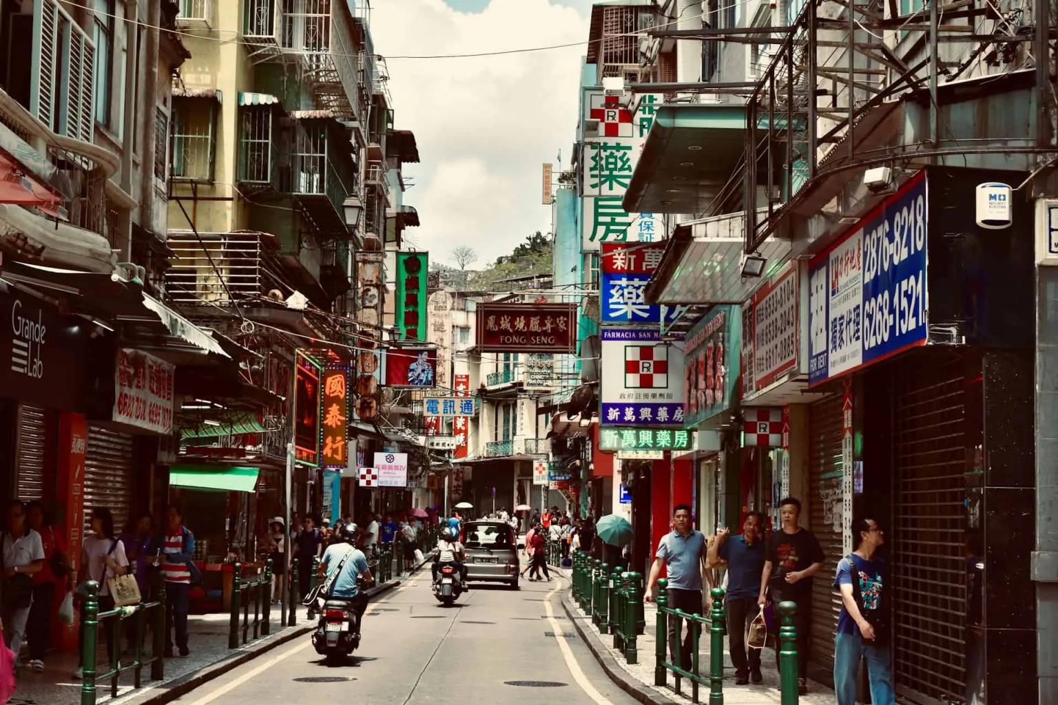Rua movimentada em Macau, com lojas e pessoas caminhando.