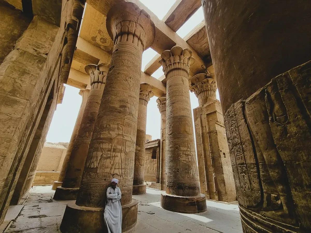 Colonne di templi dell'antico Egitto con geroglifici dettagliati e una persona in primo piano vestita in abiti tradizionali
