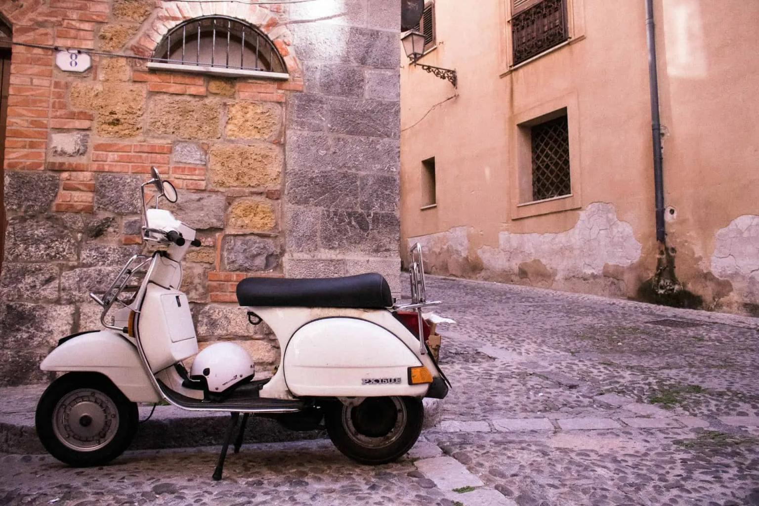 Uma vespa branca estacionada em uma rua de paralelepípedos na Sicília.