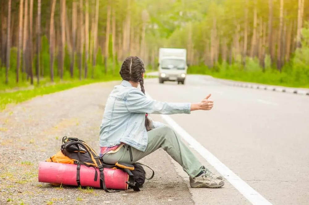 rapariga com tranças pede boleia ao pé de uma estrada