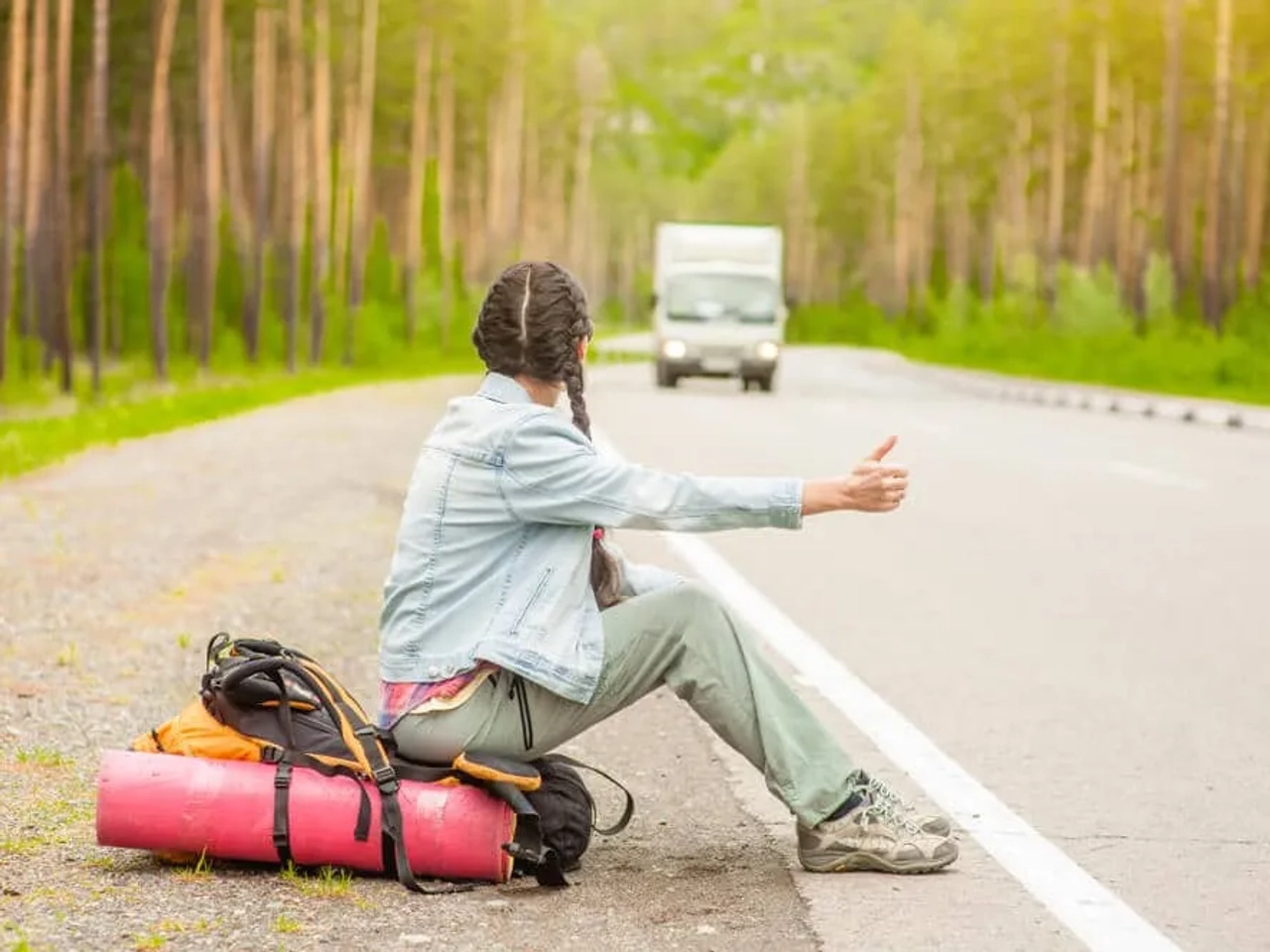 rapariga com tranças pede boleia ao pé de uma estrada