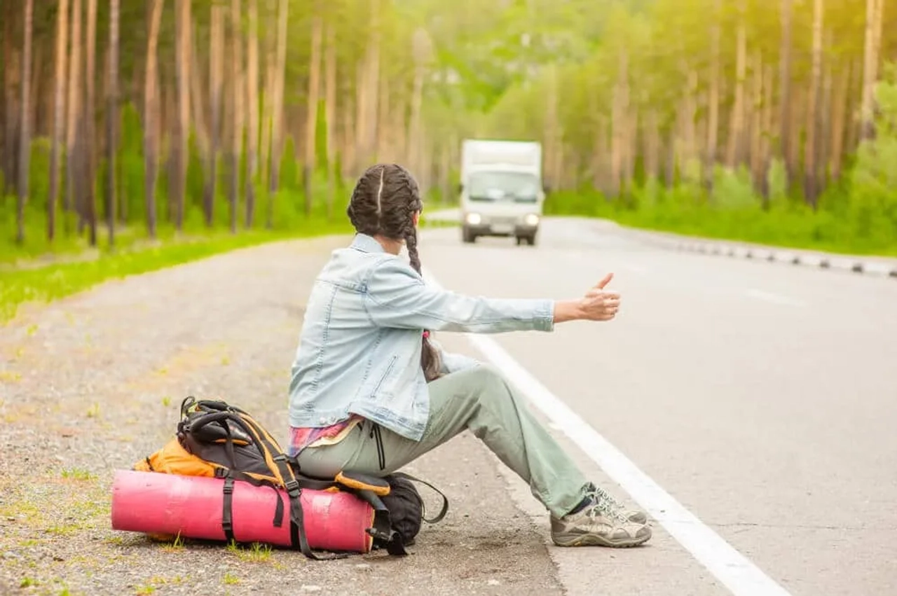 rapariga com tranças pede boleia ao pé de uma estrada