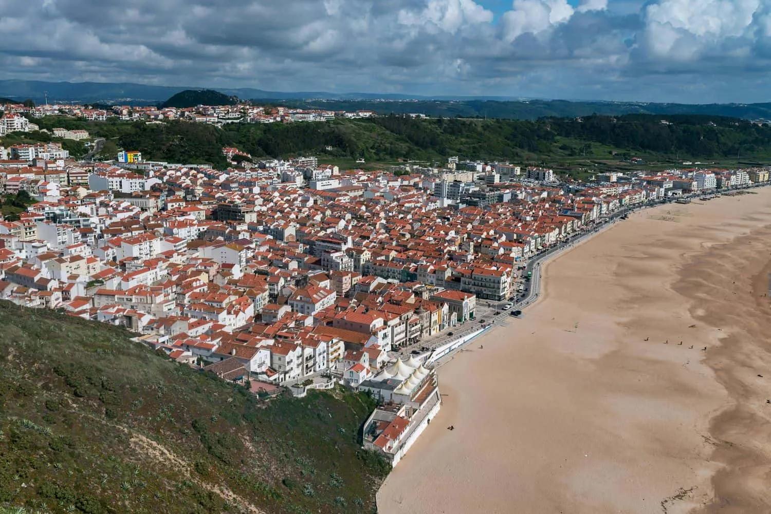Vista aérea de uma cidade costeira com praia e casas de telhado vermelho.