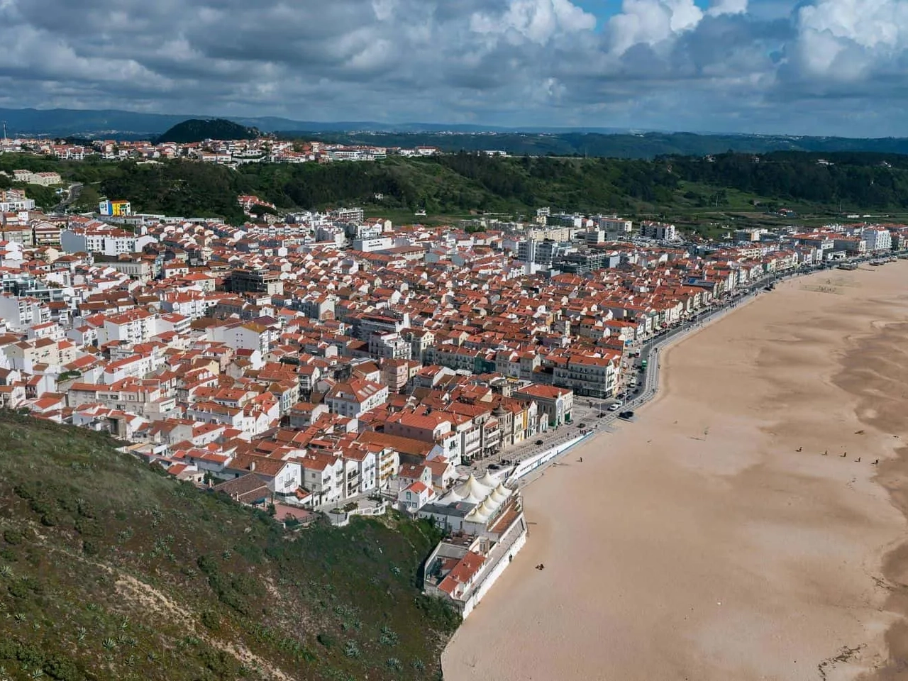 Vista aérea de uma cidade costeira com praia e casas de telhado vermelho.