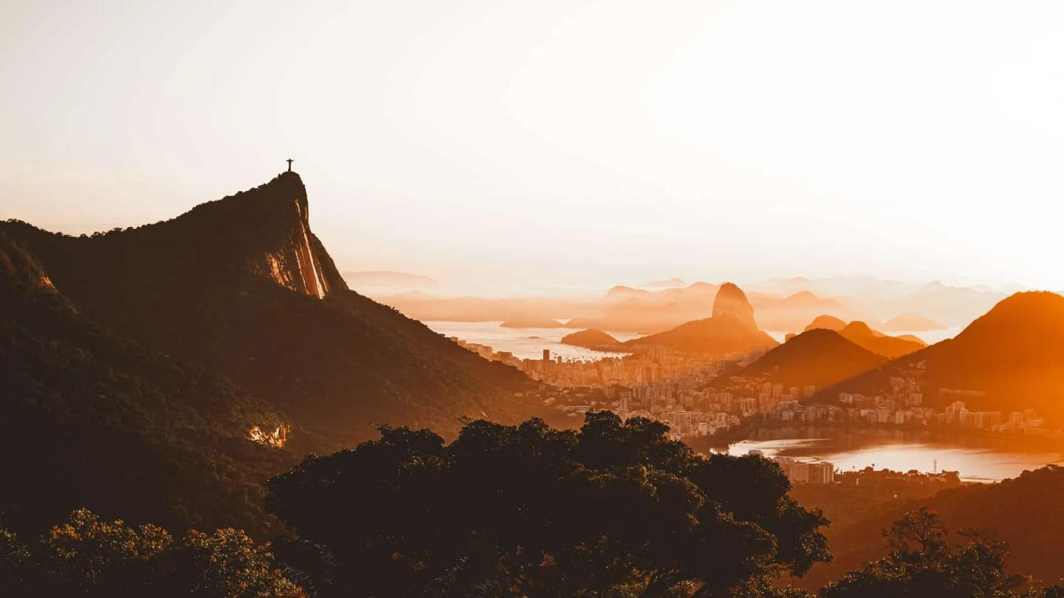 Vista do Cristo Redentor ao pôr do sol, com montanhas e cidade ao fundo.