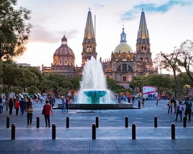 pessoas a passear junto a uma fonte e catedral ao final da tarde no méxico