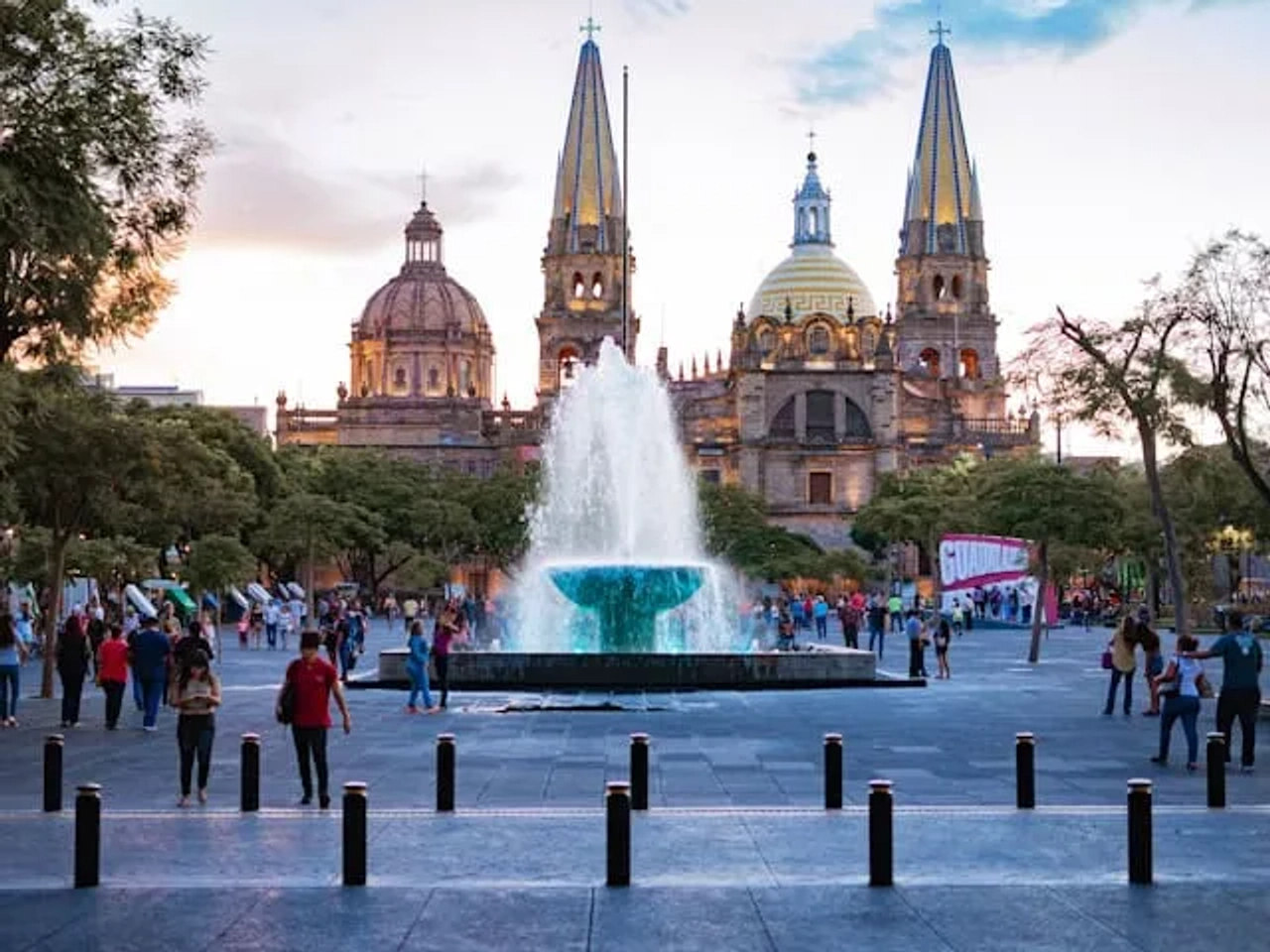 pessoas a passear junto a uma fonte e catedral ao final da tarde no méxico