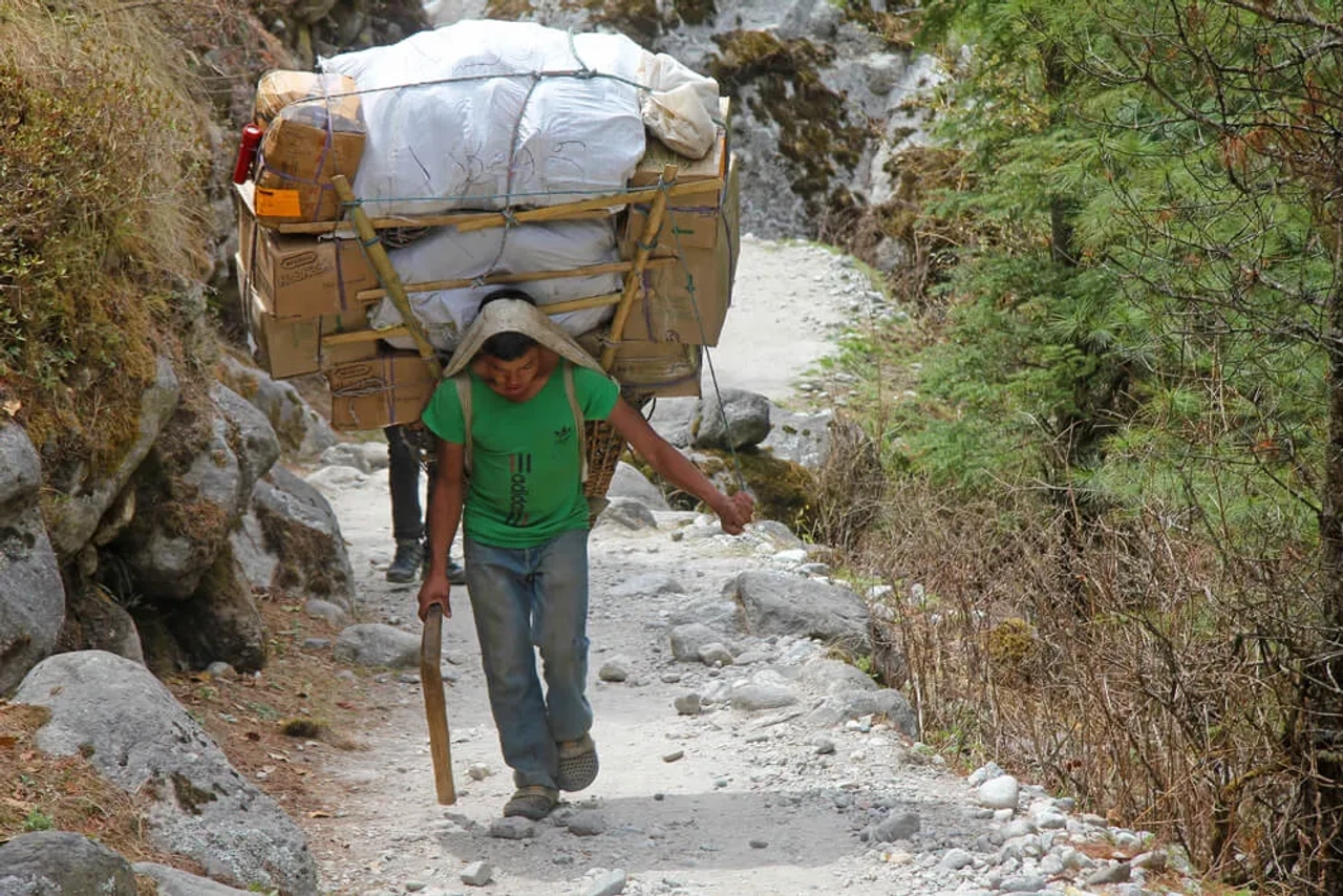 um sherpa a carregar varios fardos pela montanha acima