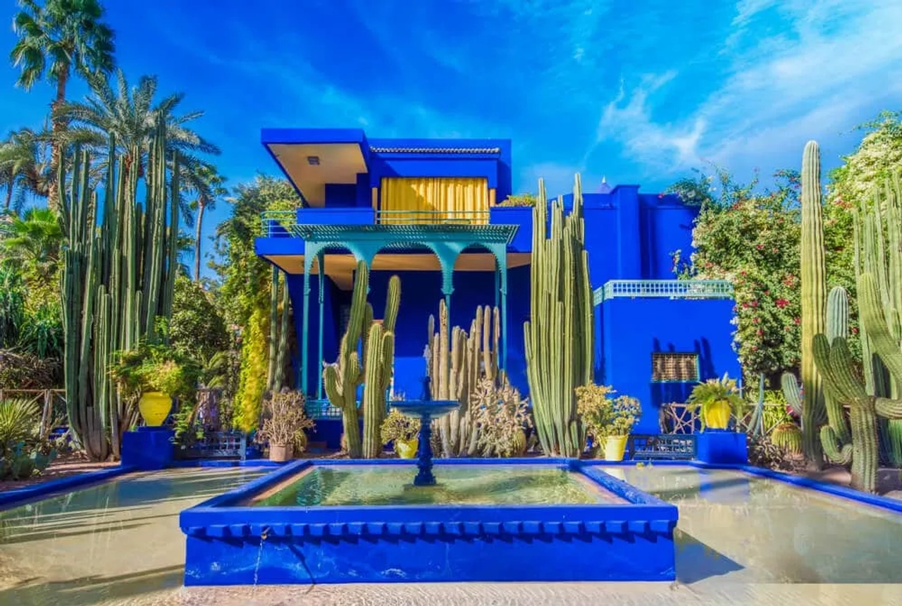 Giardino Majorelle a Marrakech, con edificio blu intenso, cactus, palme e fontana decorativa in primo piano.