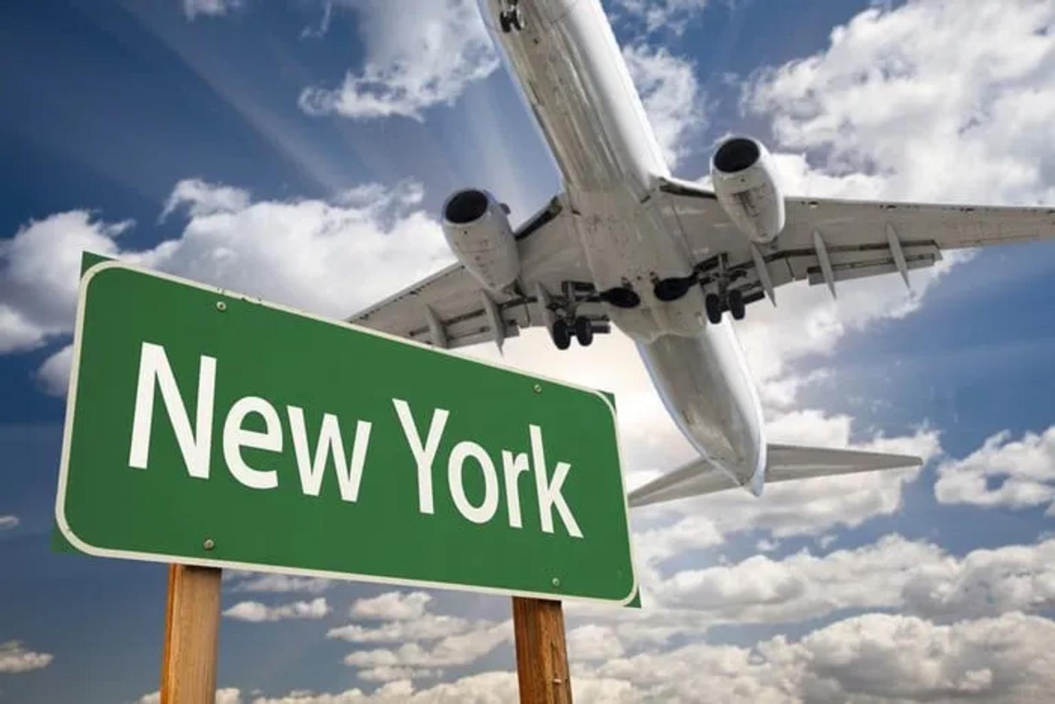 Señal de Nueva York con un avión volando sobre un cielo nublado.