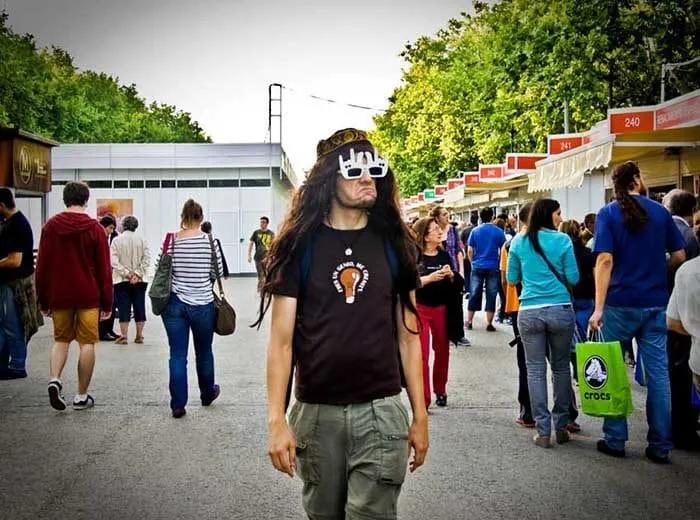 Hombre con gafas peculiares camina entre una multitud en un evento al aire libre.