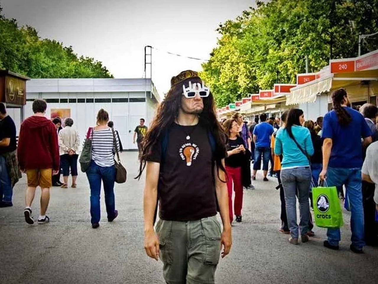 Hombre con gafas peculiares camina entre una multitud en un evento al aire libre.