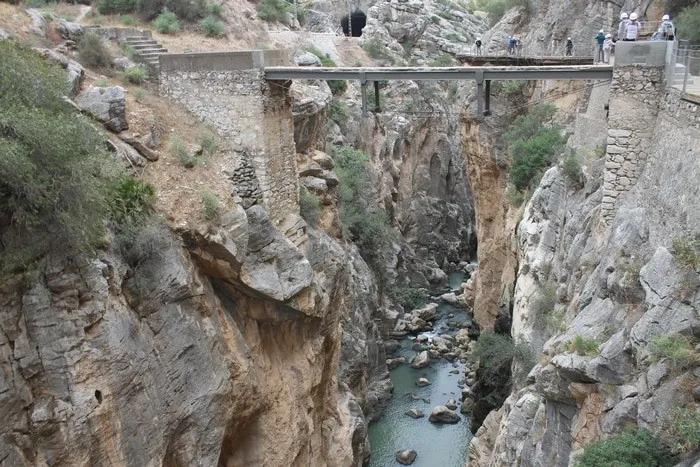 Puente sobre un cañón profundo con un río y senderistas en el fondo.
