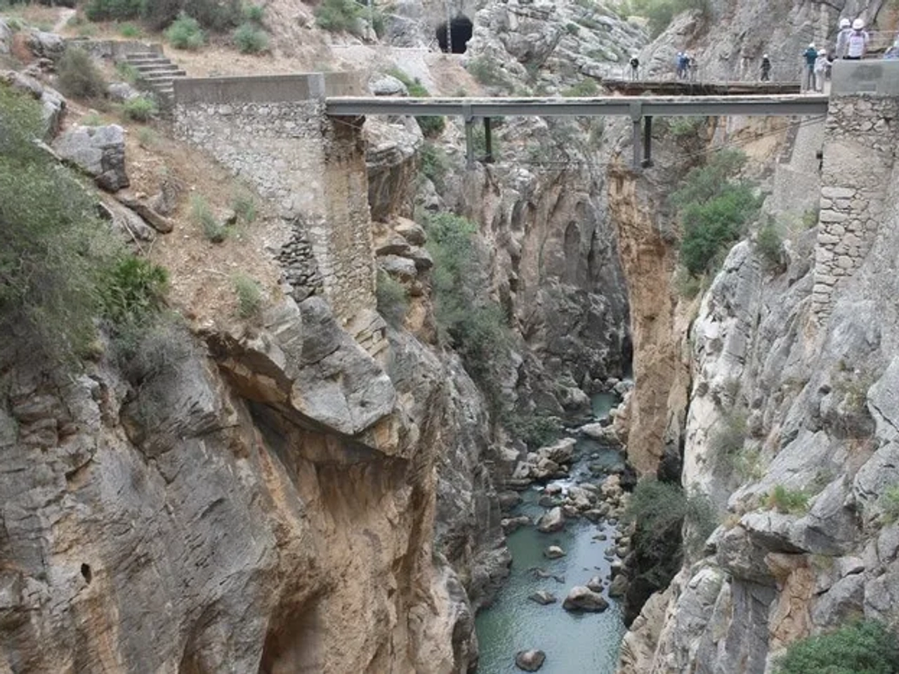 Puente sobre un cañón profundo con un río y senderistas en el fondo.