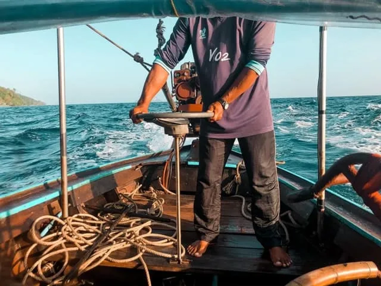 homem com calças pretas a agarrar no volante de um barco