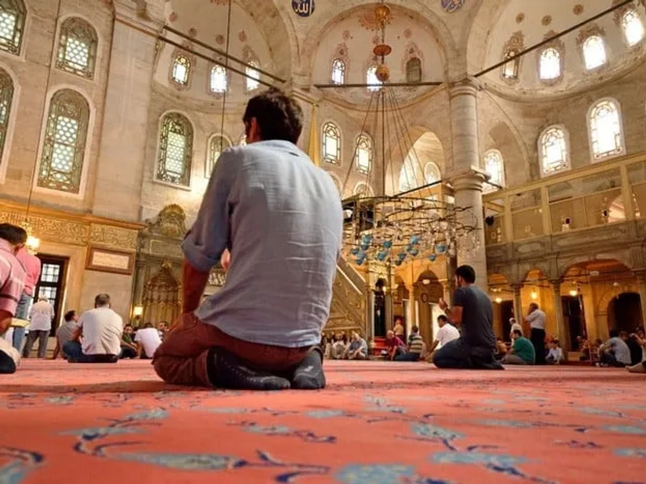 Homens orando em uma mesquita, com arquitetura rica e detalhes ornamentais.