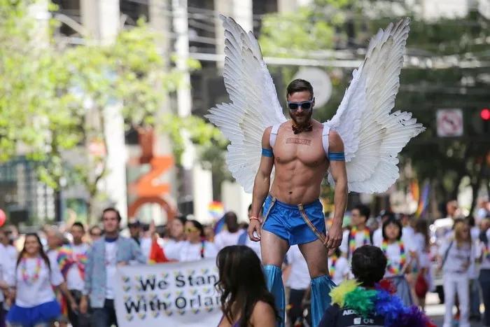 Hombre con alas en un desfile del Día del Orgullo Gay, rodeado de multitudes.