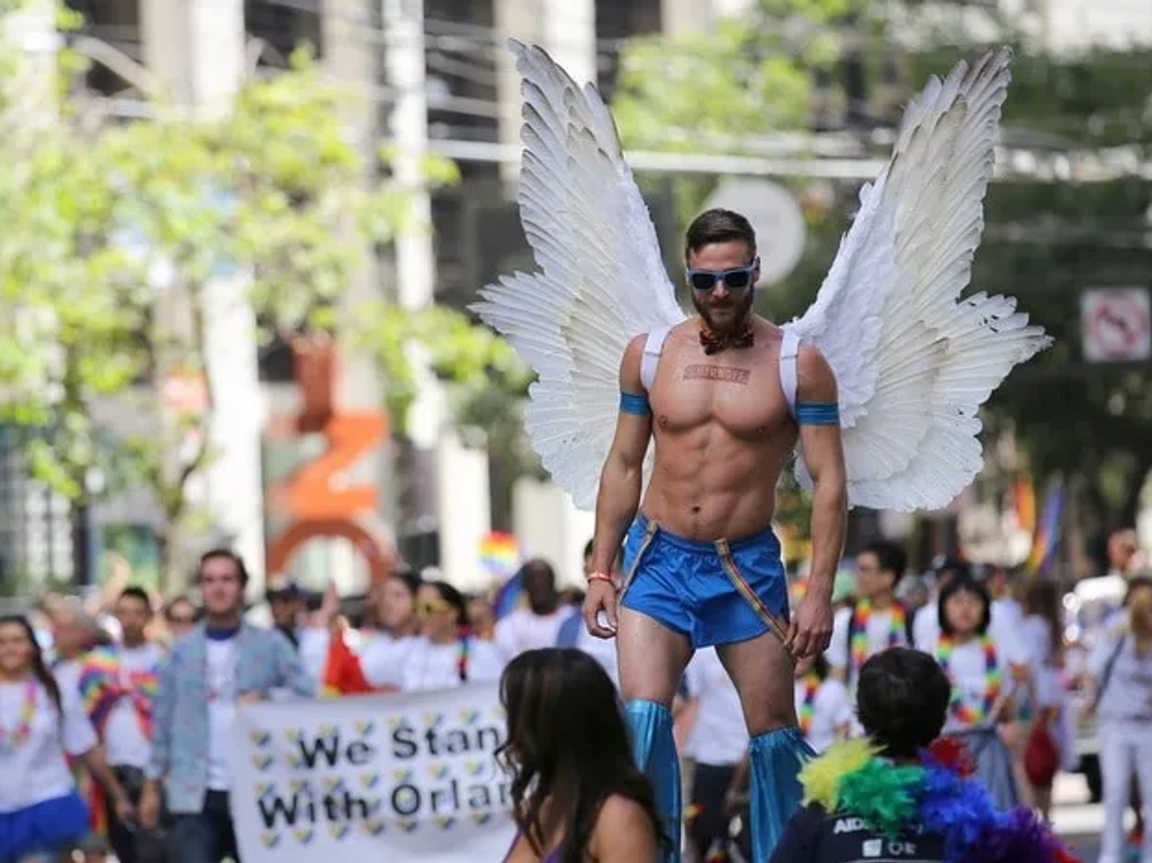 Hombre con alas en un desfile del Día del Orgullo Gay, rodeado de multitudes.