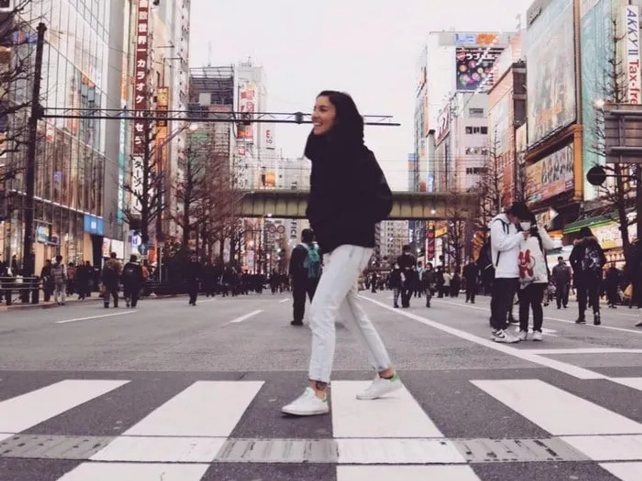 Mujer sonriente cruzando una calle concurrida en una ciudad moderna.