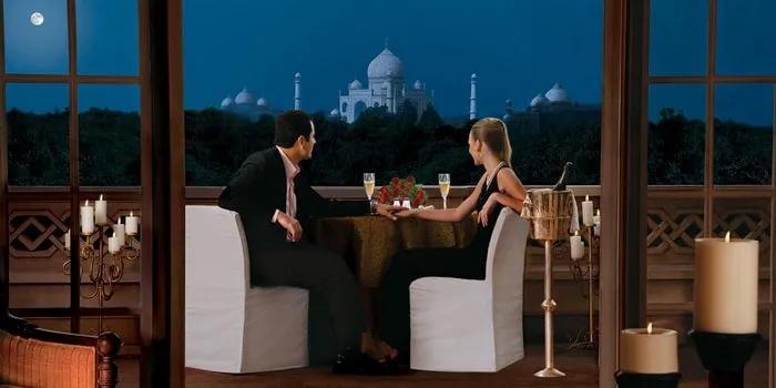 Pareja cenando en un balcón con vista al Taj Mahal iluminado por la luna.
