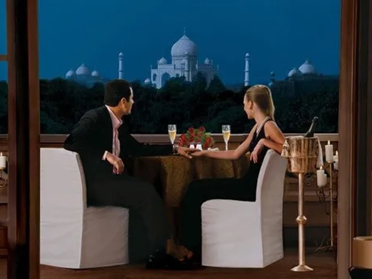 Pareja cenando en un balcón con vista al Taj Mahal iluminado por la luna.