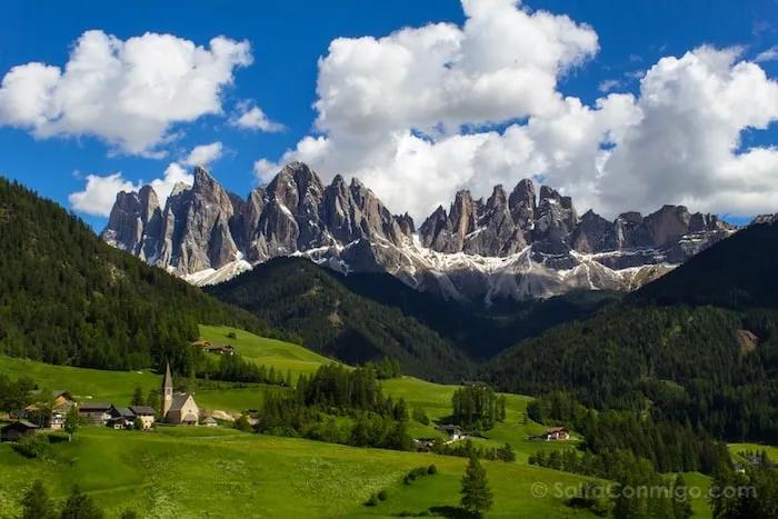 Montañas imponentes con prados verdes y un pueblo pintoresco al pie.