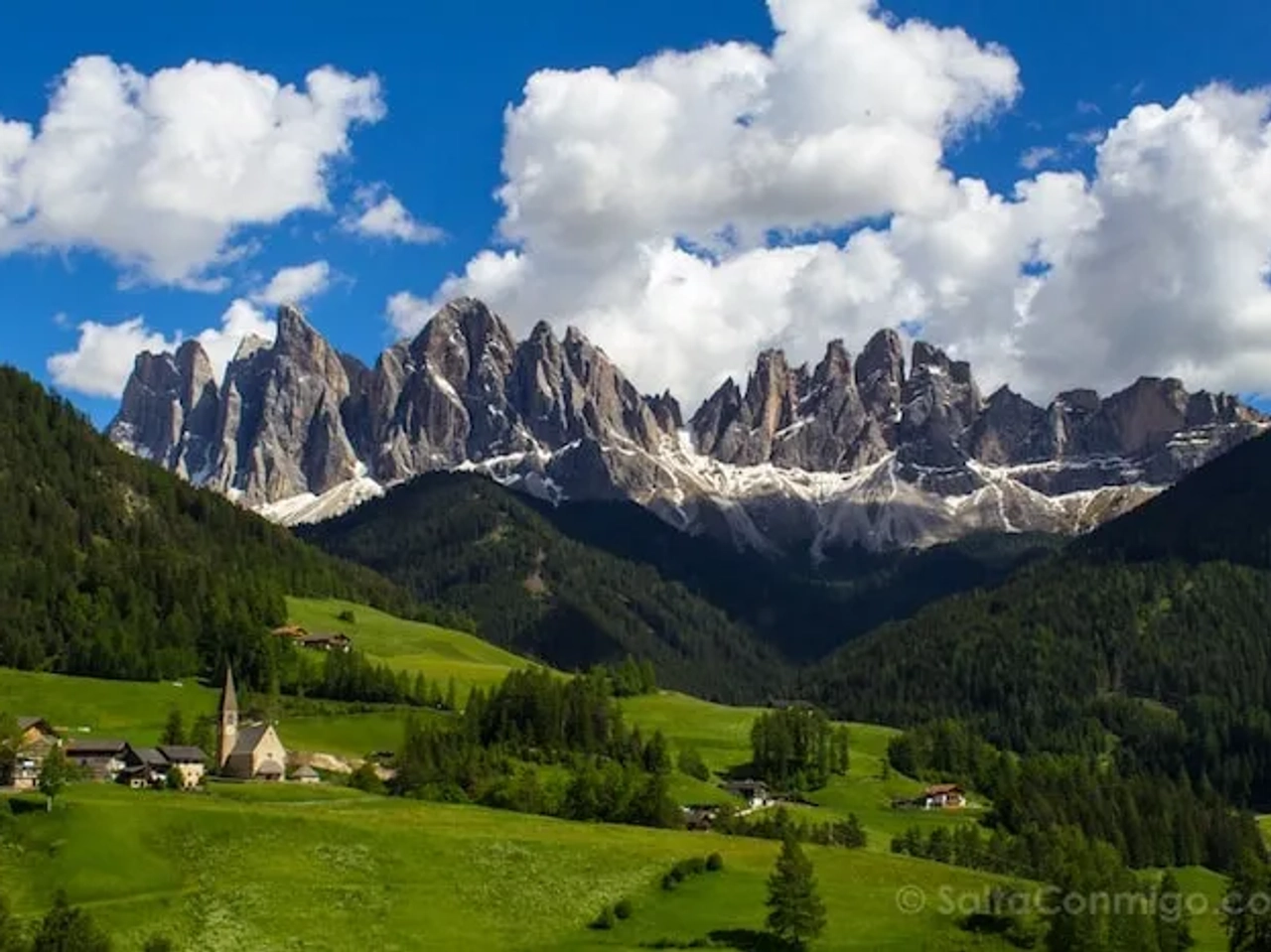 Montañas imponentes con prados verdes y un pueblo pintoresco al pie.
