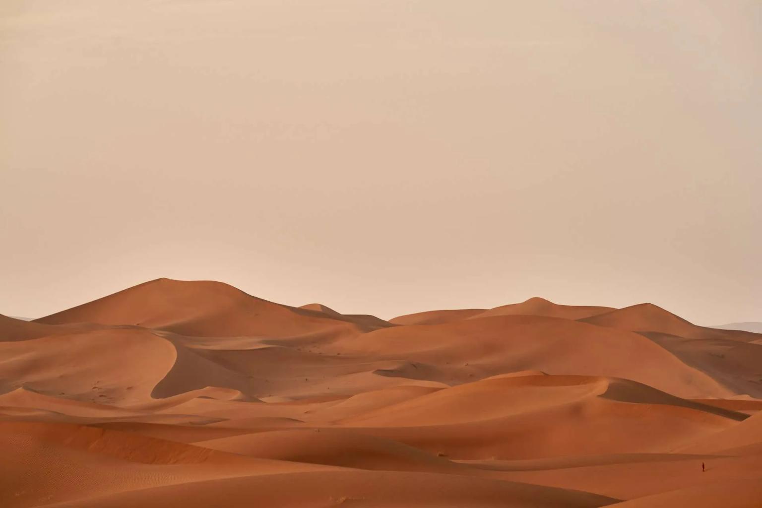 Dunas de areia avermelhadas sob um céu claro, representando o deserto do Marrocos.