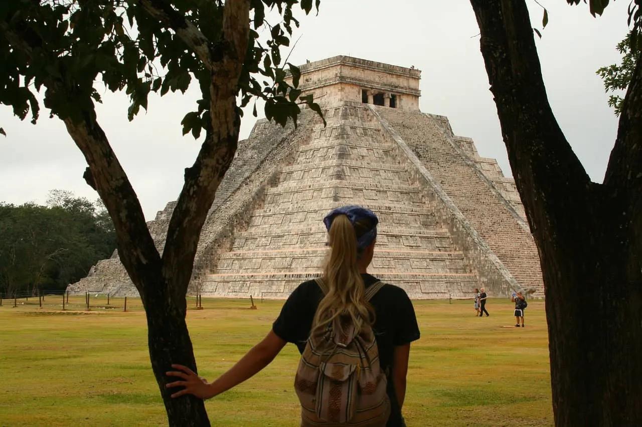 Mujer observa la pirámide de Chichén Itzá entre árboles en un paisaje verde.