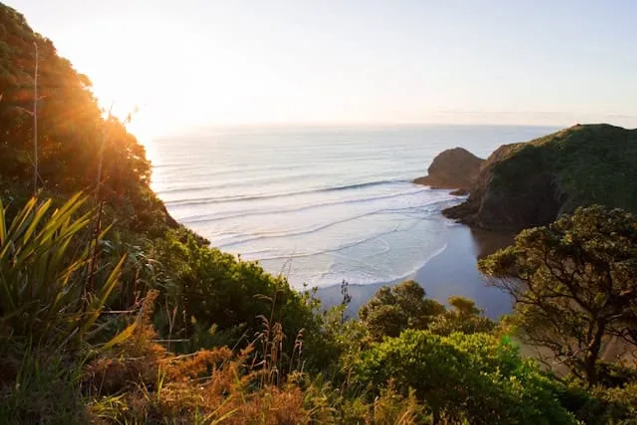monte verde junto a uma praia com o por do sol em White's Beach na Nova Zelândia