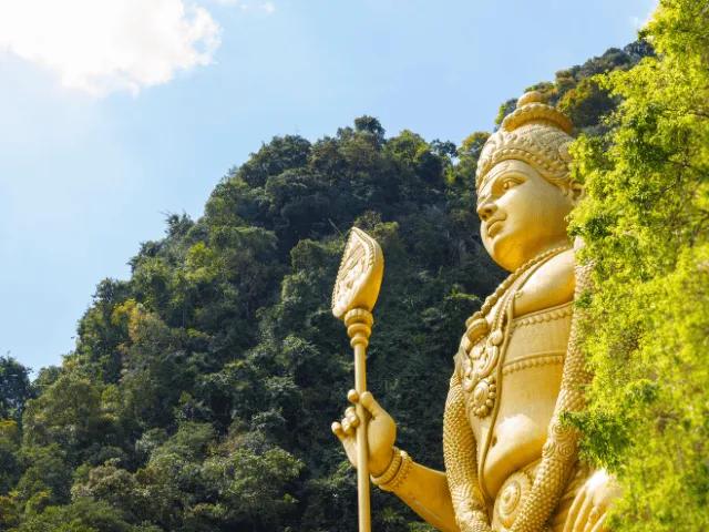 estatua em dourado de um buda a segurar numa pá no meio da floresta em Kuala Lumpur no sudeste asiatico