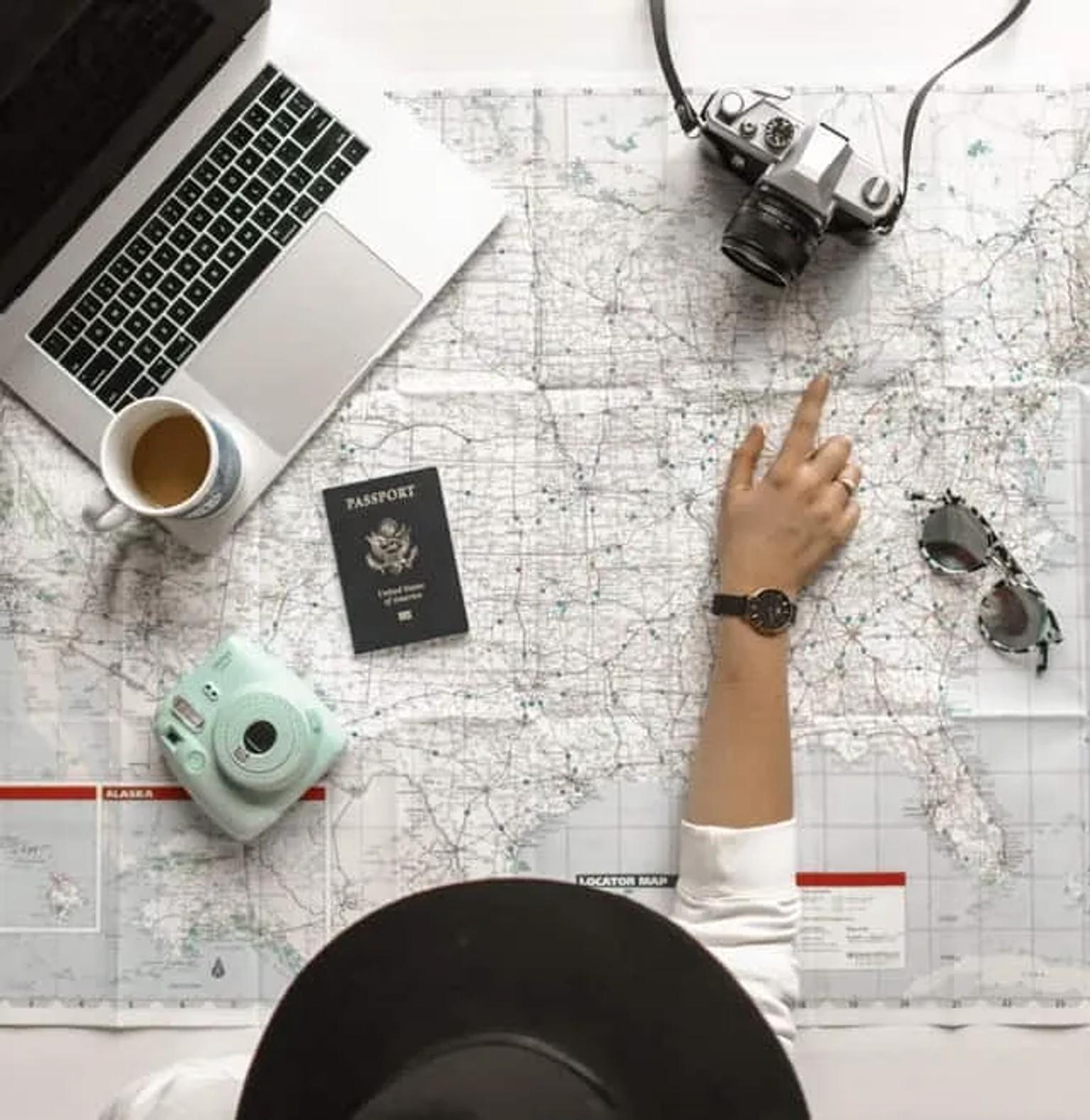 Pessoa planejando viagem com mapa, passaporte, laptop e câmera.