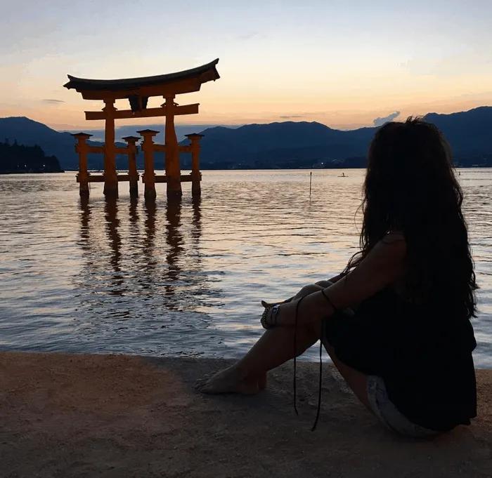 Mujer contemplando un torii en el agua durante el atardecer.